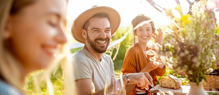 Three smiling people sitting at an outdoor dinner setting.