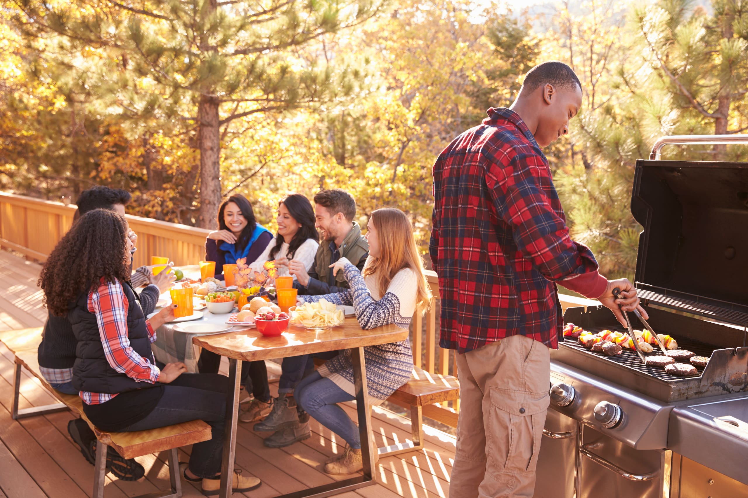 Outdoor dinner scene with someone at the barbecue in the foreground