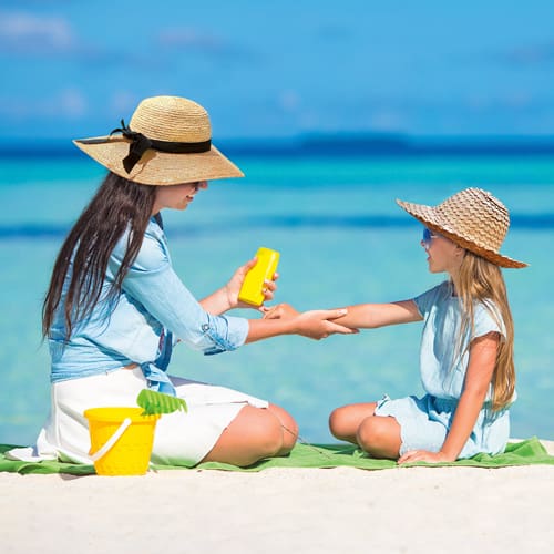 mom and daughter at the beach putting on sunscreen