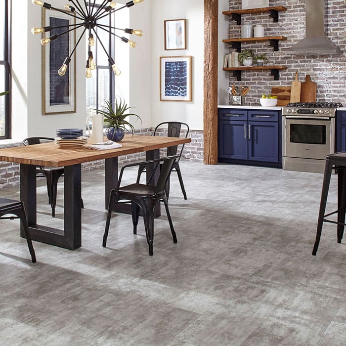 A bright, modern farm-house styled kitchen, with a trendy chandelier over a wood-top table. Gray and white vinyl flooring is predominantly featured.