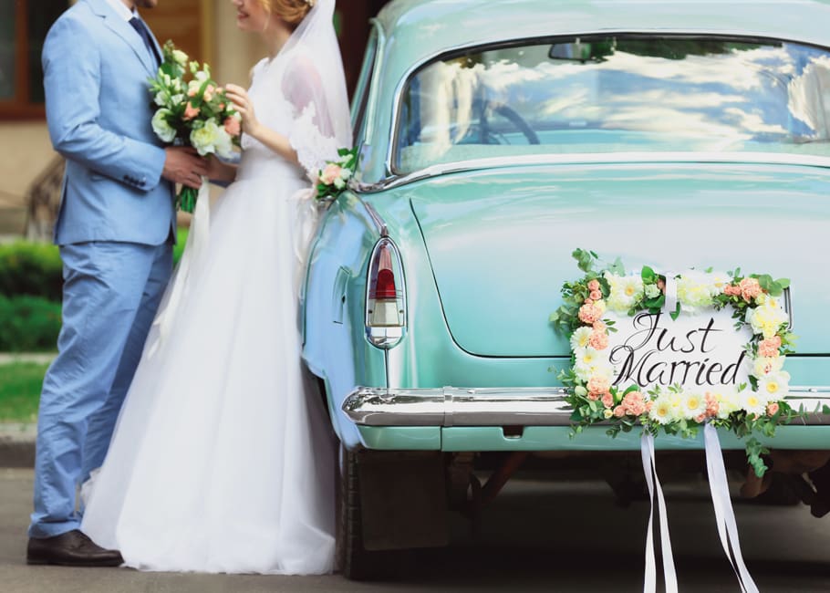 groom and bride leaning against vintage car