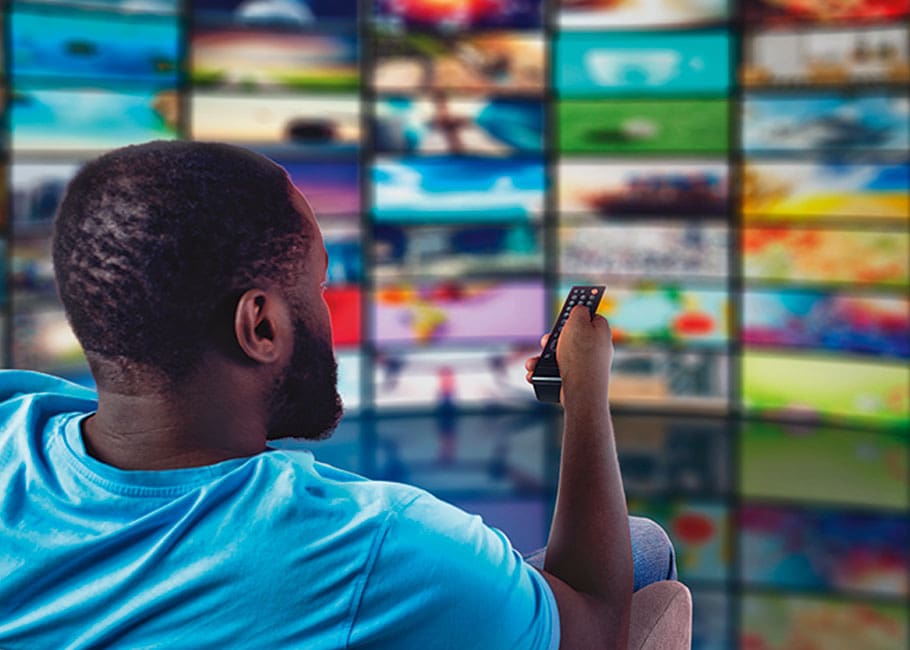 man with remote in front of wall of tvs