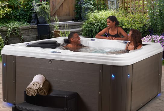 Three people chat and sit in a hot tub.