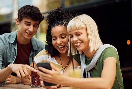 A trio of friends at a table looking at a phone together.